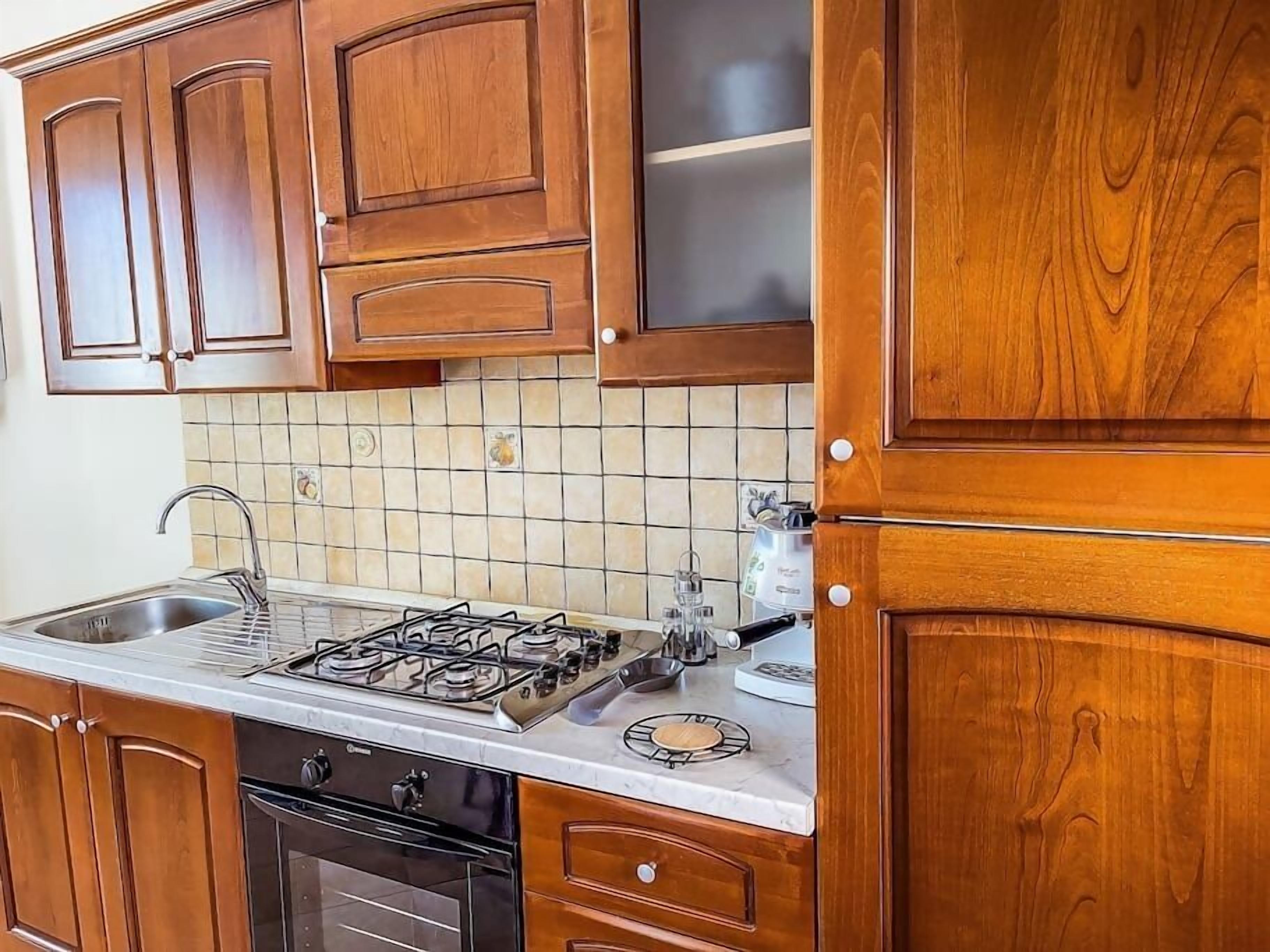 Una cocina con gabinetes de madera, una estufa a gas, un fregadero y salpicadero de azulejos.