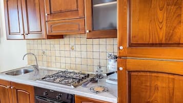 Una cocina con gabinetes de madera, una estufa a gas, un fregadero y salpicadero de azulejos.