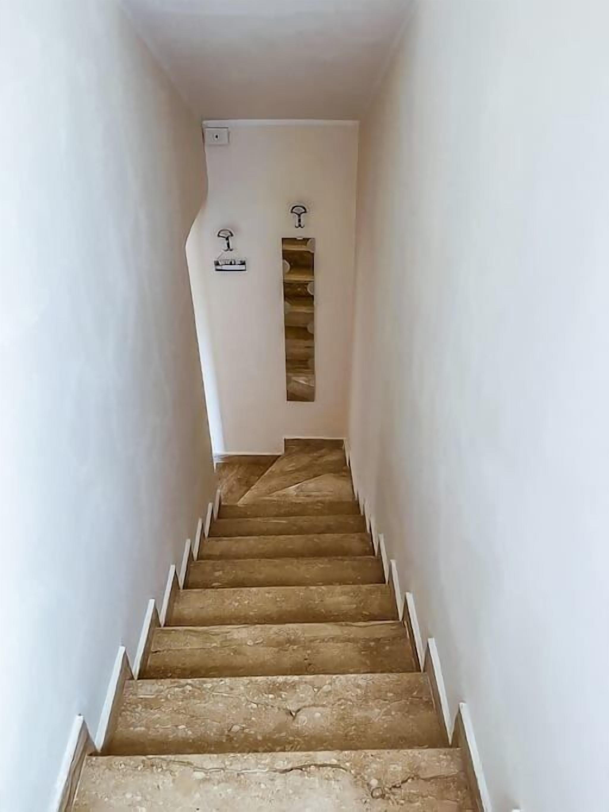 Una escalera estrecha con escalones de madera y paredes blancas, que conduce a una habitación con estantería empotrada.