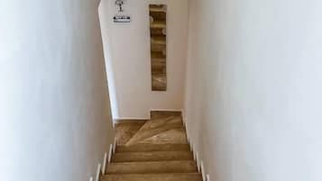 Una escalera estrecha con escalones de madera y paredes blancas, que conduce a una habitación con estantería empotrada.