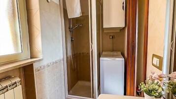 Une salle de bain avec une douche, un lavabo, une fenêtre et un meuble de rangement.