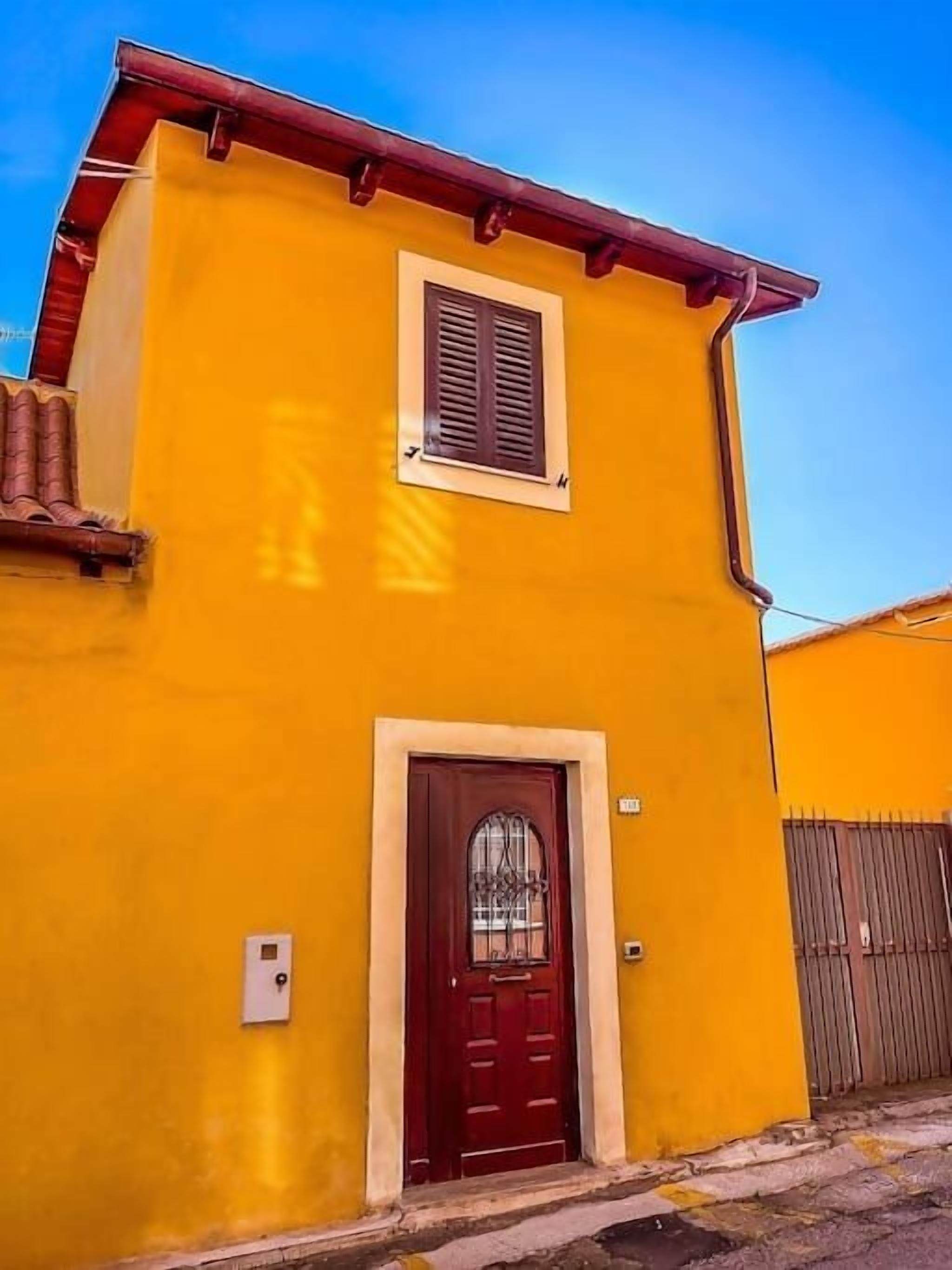 Un edificio de dos pisos con una puerta roja y una ventana pequeña.