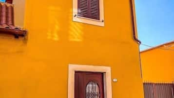 Un edificio de dos pisos con una puerta roja y una ventana pequeña.
