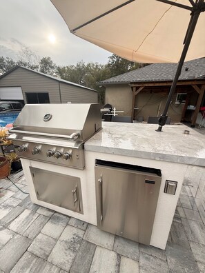 An outdoor kitchen with a grill, a sink, and a built-in refrigerator. - The Lion's Den, Studio guest house. (Orange City)