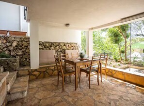 A stone-floored patio with a wooden table and chairs, a stone wall, and a view of greenery outside. - Blue Magic Apartment - Two Bedroom Apartment with Sea View and Terrace (Seget Vranjica)