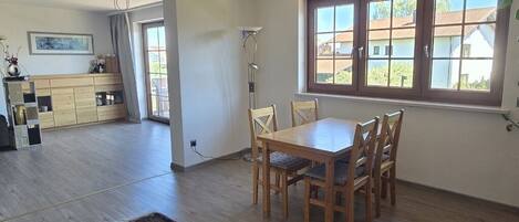 Un coin repas avec une table et des chaises en bois, une grande fenêtre offrant une belle vue et un espace cuisine avec des placards en bois.