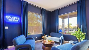 Una habitación moderna con paredes oscuras, un letrero de neón que dice 'SQUEEZE THE DAY' y ventanas grandes con cortinas.