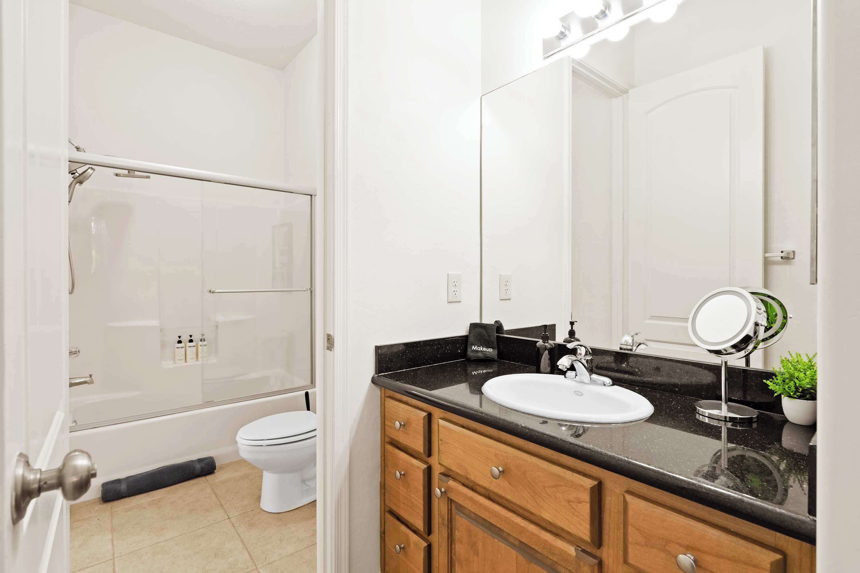 A bathroom with a bathtub, toilet, vanity with a sink, mirror, and a potted plant.