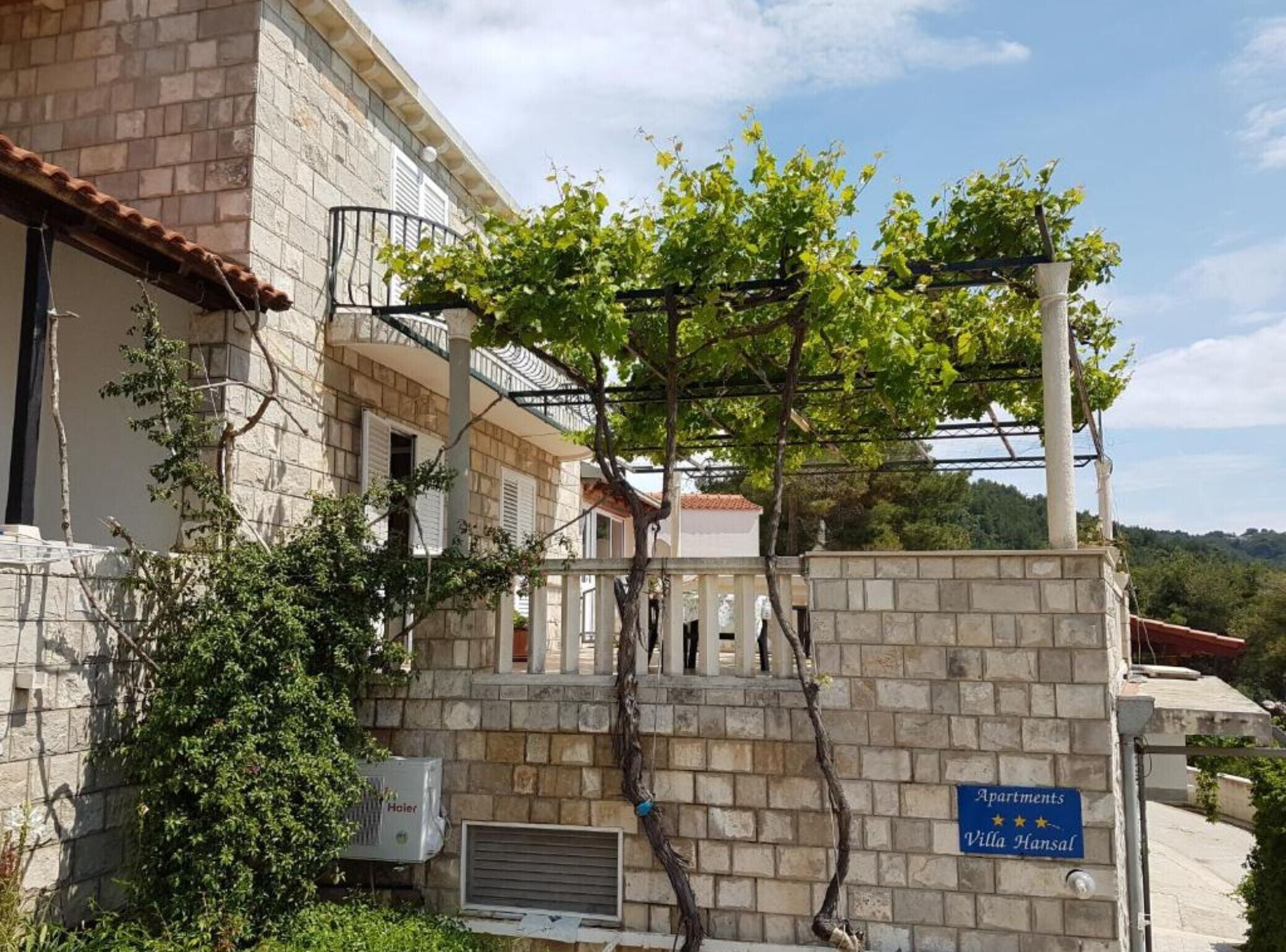 Un immeuble aux murs de pierre, doté d’un balcon et d’une enseigne indiquant « Appartements Villa Hansal ».