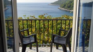 Ein Balkon mit zwei Stühlen und Blick auf das Meer sowie eine hügelige Landschaft.