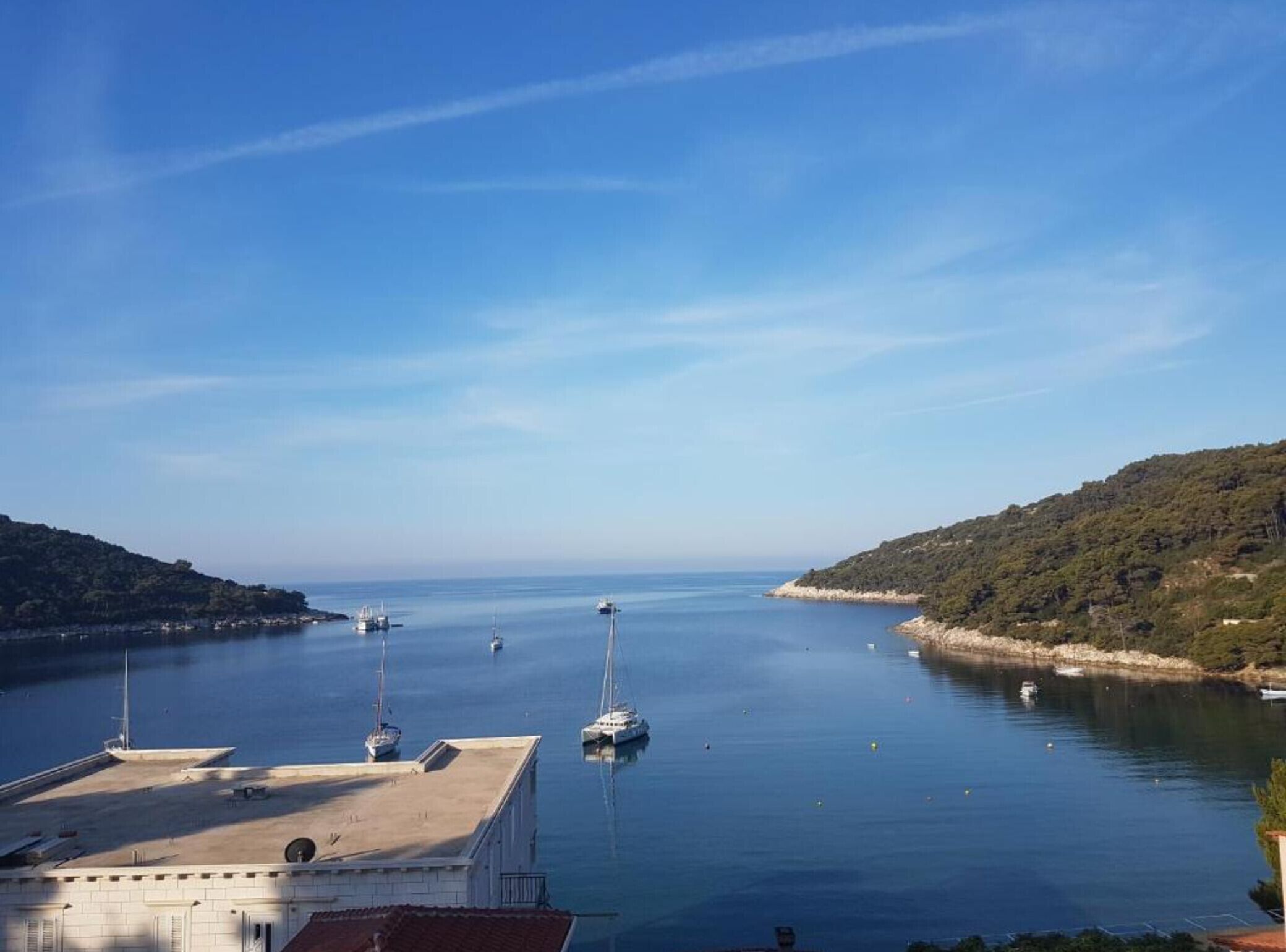 Un port de plaisance avec des bateaux amarrés, un ciel dégagé et un paysage vallonné en arrière-plan.