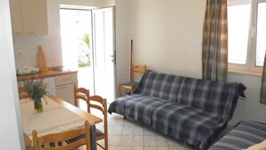 A small, cozy room with a sofa, a dining table with chairs, a kitchen area with cabinets, and a window with curtains. - Villa Azure Saplunara - One bedroom apartment Mirta (Saplunara)