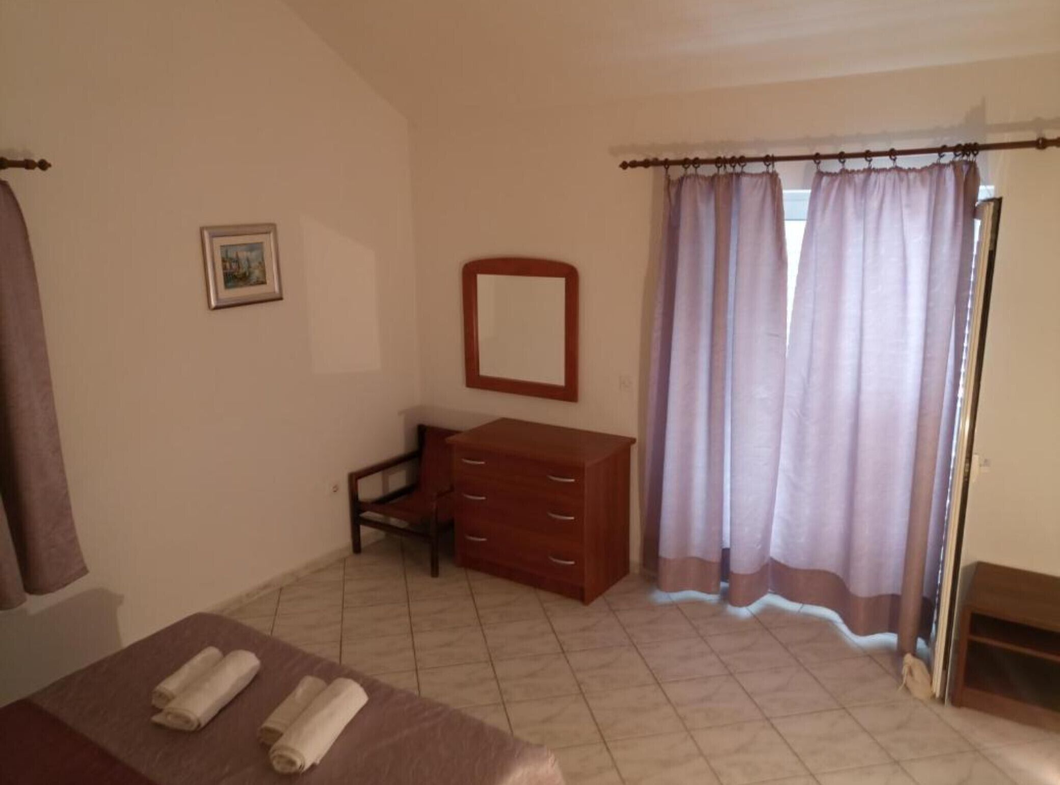 Un dormitorio con cama, cómoda, silla, espejo y ventana con cortinas.