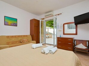 Ein Schlafzimmer mit einem Bett, einem Holzschrank, einer Holzkommode, einem Fernseher und einer Glastür, die zu einem Außenbereich führt.