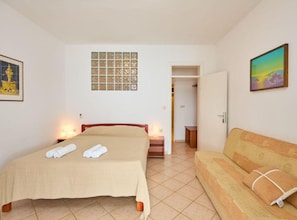Ein Schlafzimmer mit einem Bett, einer Couch, einem kleinen Tisch, einem Fenster mit Aussicht und einer Tür zu einem anderen Raum.