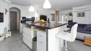 Cocina moderna con una isla central, armarios blancos e iluminación colgante.