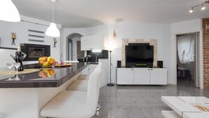 Una cocina moderna con una isla central, armarios blancos y un televisor de pantalla plana montado sobre una pared de acento de piedra.