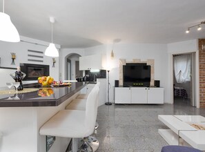 Eine moderne Küche mit einer zentralen Kochinsel, weißen Schränken und einem Flachbildfernseher an einer Steinwand.