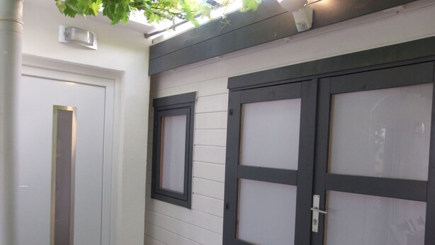 Una porta bianca con una striscia verticale, una finestra con cornice scura e un portone garage con pannello vetro smerigliato.