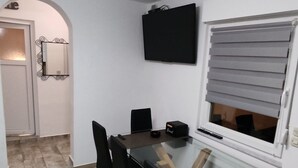 Un'area pranzo con un tavolo in vetro, sedie nere, un altoparlante nero e una finestra con persiane.