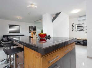 Eine moderne Küche mit Kochinsel, Barhocker und einer Essecke mit einer Couch.