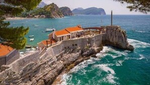 Ein Küstenhaus aus Stein mit rotem Dach, das auf einer felsigen Klippe über dem Meer thront.
