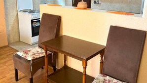 Cocina compacta con estufa, lavamanos y armarios. Hay una mesa de comedor con dos sillas.