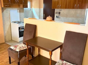 Cocina compacta con estufa, lavamanos y armarios. Hay una mesa de comedor con dos sillas.