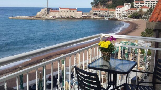Un balcón con mesa y sillas que da a una playa y una fortaleza histórica.