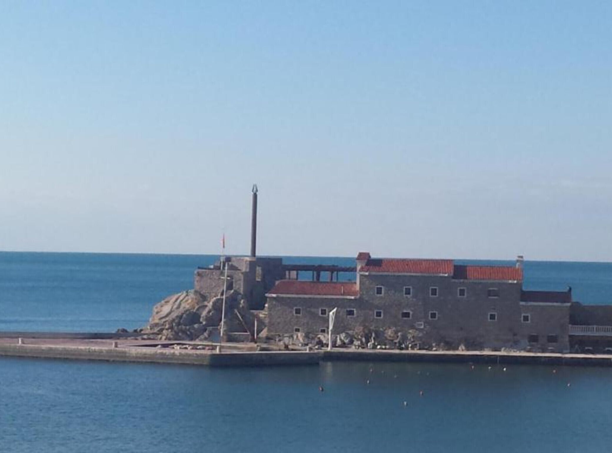 A coastal building with a red roof, a flagpole, and a lighthouse.