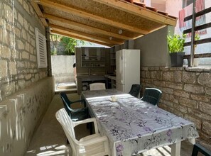 Uma área de refeições ao ar livre coberta, com mesa, cadeiras, churrasqueira embutida e paredes de pedra.