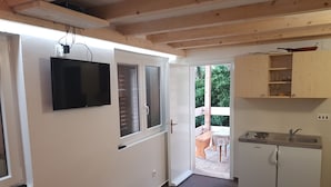 Eine Küche mit Spüle, Schränken und einem Fernseher. Eine Tür führt zu einem Außenbereich mit Tisch und Stühlen.