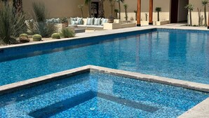 Une piscine ornée de mosaïques, un espace détente avec un canapé et des coussins, ainsi que diverses plantes.