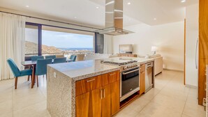 Une cuisine moderne dotée d’un grand îlot central, d’un four encastré et offrant une vue sur l’extérieur.