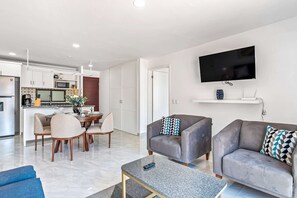 Ein modernes Wohnzimmer mit Flachbildfernseher, grauen Sofas, einem Couchtisch und einem Essbereich mit Stühlen und einem Tisch.