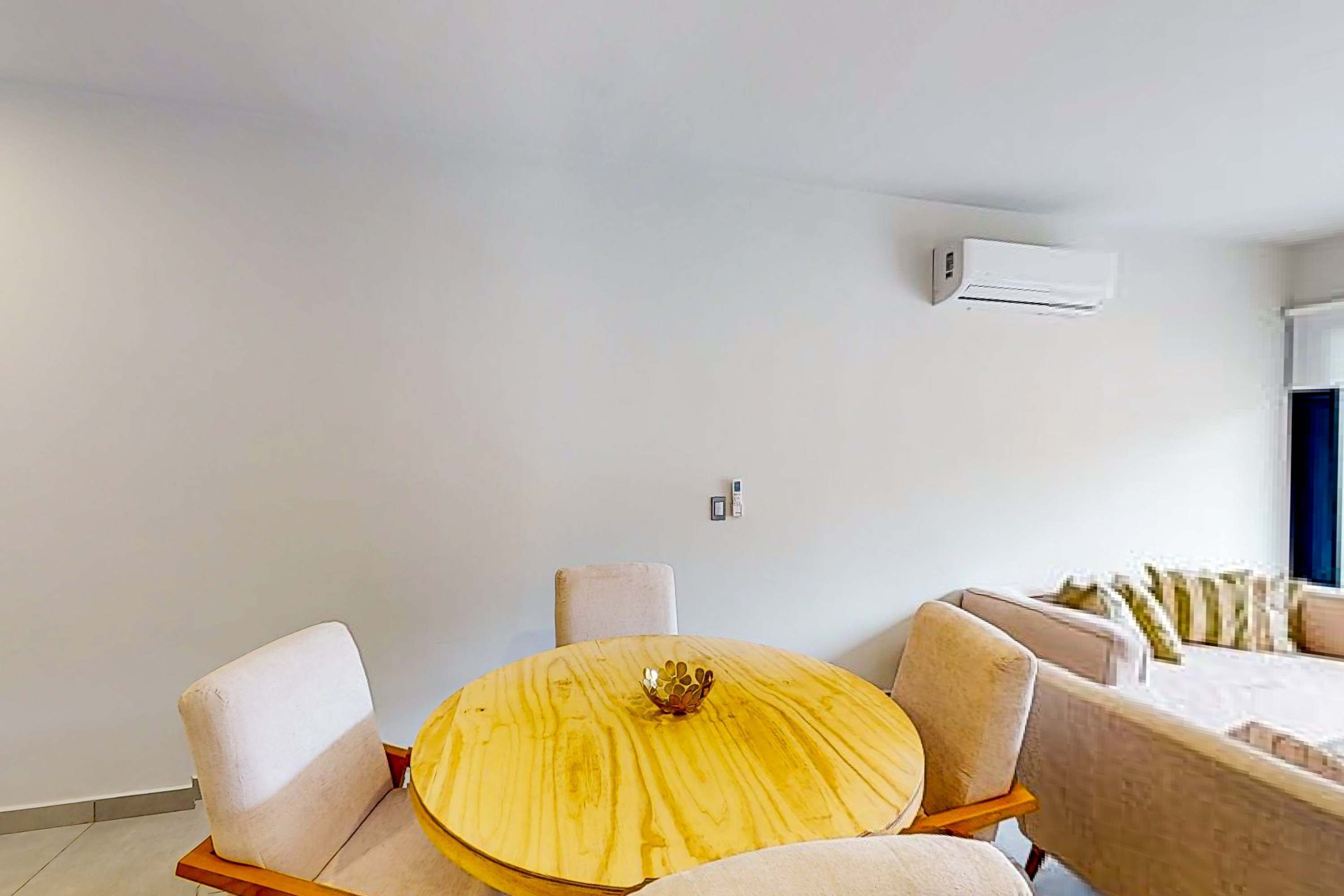 Ein modernes Zimmer mit einem runden Holztisch, vier Stühlen, einer Couch und einer Klimaanlage.