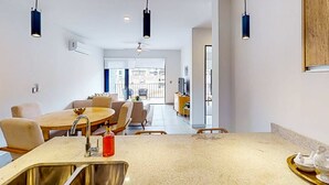 A modern kitchen with a central island, overhead pendant lights, and a dining area with chairs and a table. - Gorgeous & Spacious Apartment with Balcony, Heated Pool - AC (Cabo San Lucas)