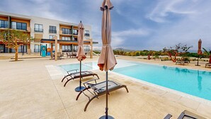 A swimming pool with lounge chairs and umbrellas, a building with balconies, and a clear sky. - Gorgeous & Spacious Apartment with Balcony, Heated Pool - AC (Cabo San Lucas)