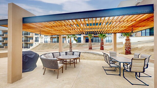 An outdoor patio area with a wooden pergola, seating arrangements, and a view of the surrounding buildings. - Gorgeous & Spacious Apartment with Balcony, Heated Pool - AC (Cabo San Lucas)