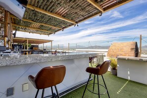 A rooftop bar with a stone wall, bar stools, and a TV. - Hotel suite with ocean-view rooftop infinity pool, balconies & AC - dog-friendly (Cabo San Lucas)