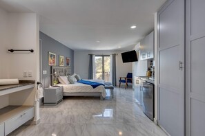 A modern bedroom with a bed, bedside tables, a desk, a flat-screen TV, and a built-in wardrobe. - Hotel suite with ocean-view rooftop infinity pool, balconies & AC - dog-friendly (Cabo San Lucas)