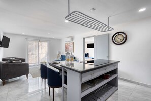 A modern kitchen with a central island, a dining area with a sofa and chairs, and a large window providing natural light. - Hotel suite with ocean-view rooftop infinity pool, balconies & AC - dog-friendly (Cabo San Lucas)