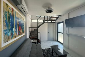 Ein modernes Wohnzimmer mit grauem Sofa, einem großen abstrakten Gemälde, einer Treppe und einem flachbildfernseher an der Wand.