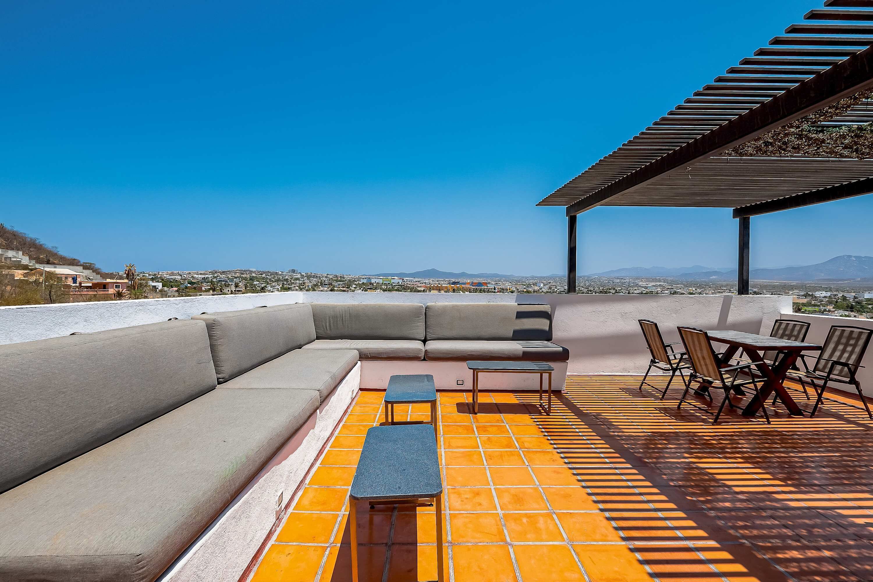Una terraza en la azotea con un sofá modular, una mesita y sillas, que ofrece vistas a la ciudad.