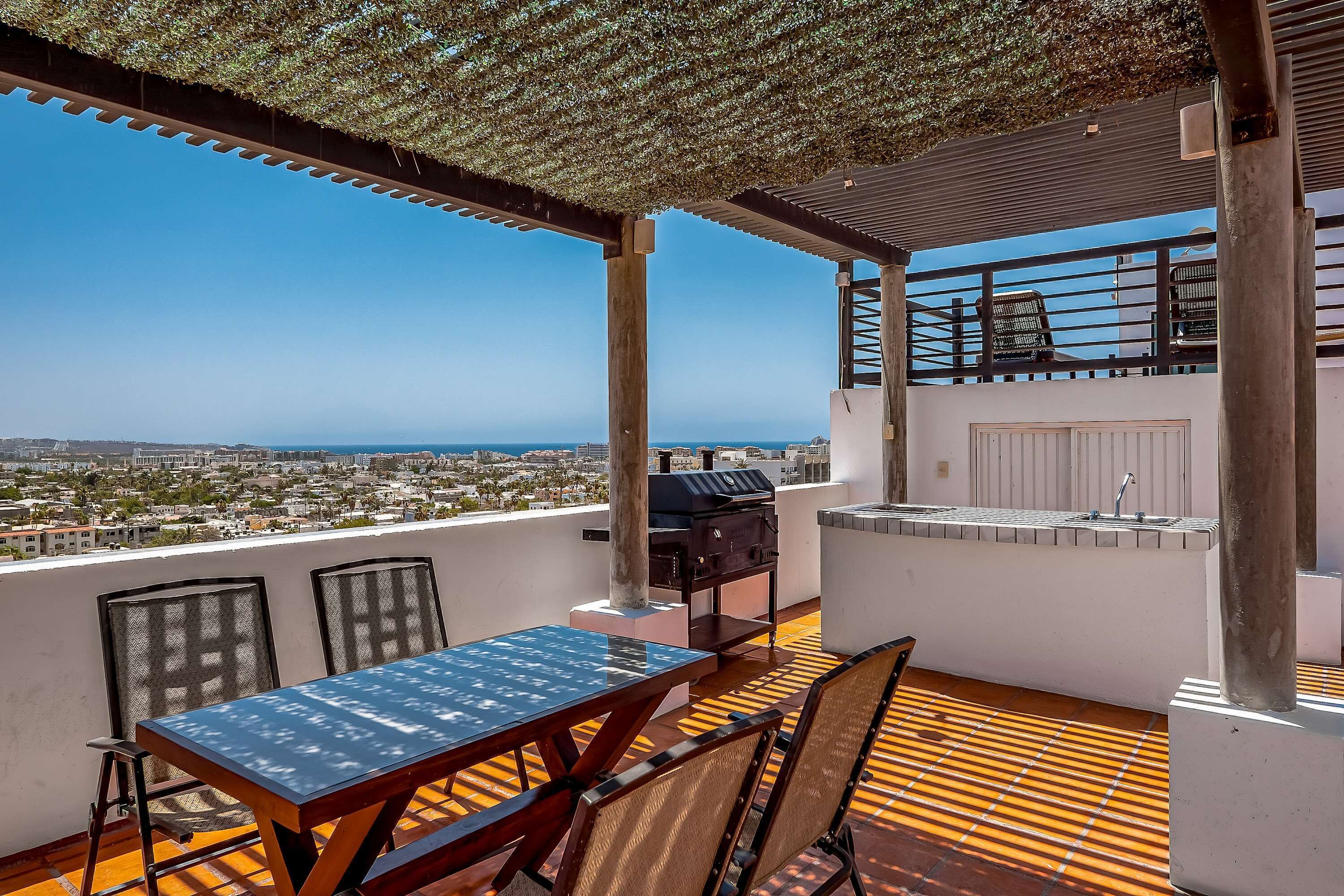 Una terraza en la azotea con mesa, sillas, una parrilla y vistas de la ciudad.