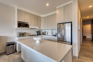 A modern kitchen with a central island, stainless steel appliances, and light wood cabinetry. - Peaceful coastal stay with pool, balcony & fitness center (Cabo San Lucas)