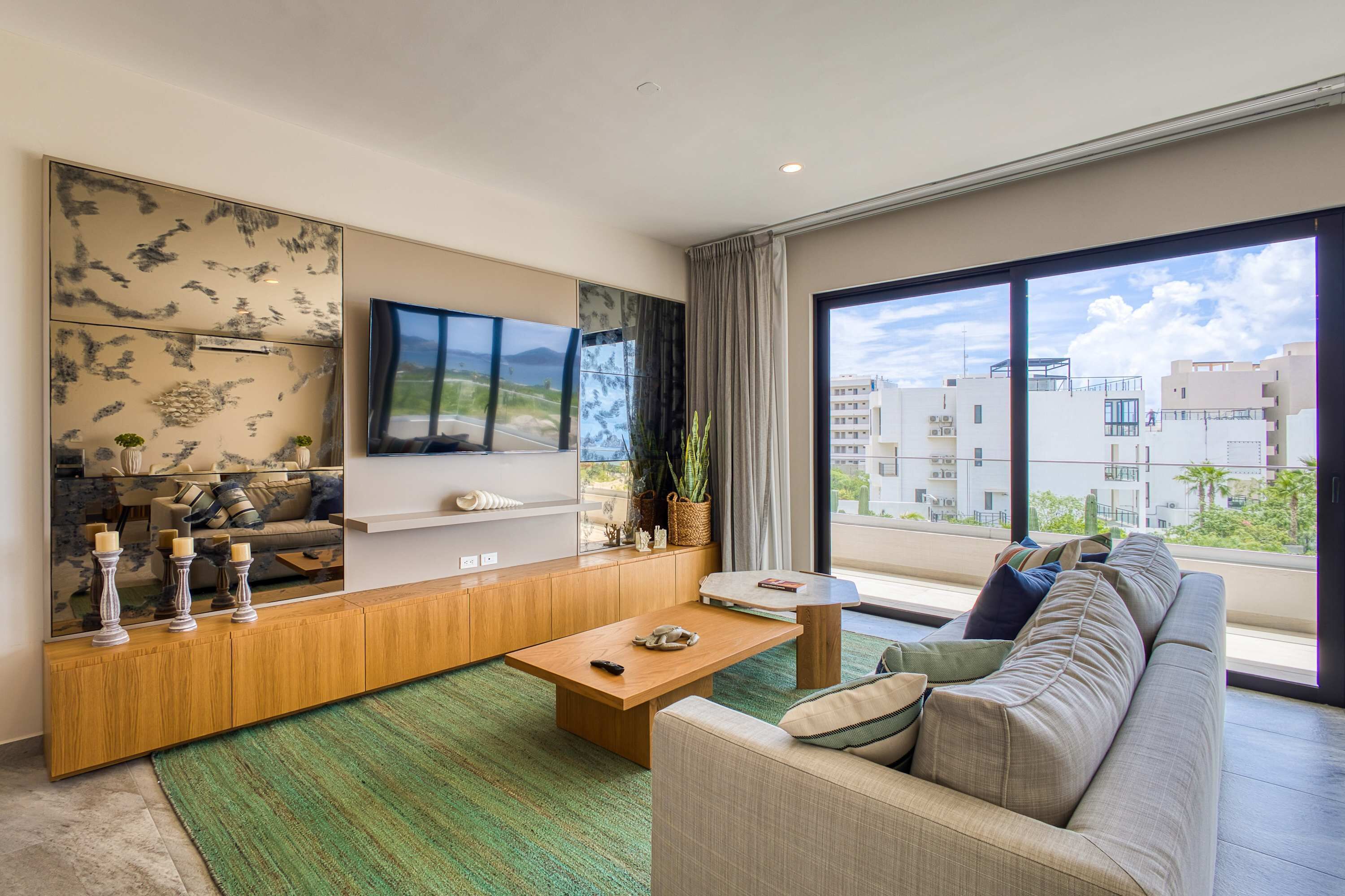 Ein modernes Wohnzimmer mit einer Couch, einem Couchtisch, einem Fernseher und großen Fenstern mit Blick auf die Stadt.