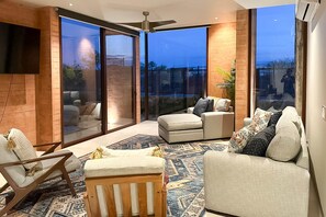 A modern living room with a large glass door leading to a balcony, a ceiling fan, and a flat-screen TV mounted on the wall. - Luxury house with private pool, ocean view, inviting balcony & elegant charm (San José del Cabo)
