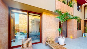 Ein modernes Gebäude mit Glastür, einem Balkon mit Sofa und Kissen sowie einer Kübelpalme.
