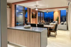 A modern living room with a dining area, large windows, and a ceiling fan. - Luxury house with private pool, ocean view, inviting balcony & elegant charm (San José del Cabo)